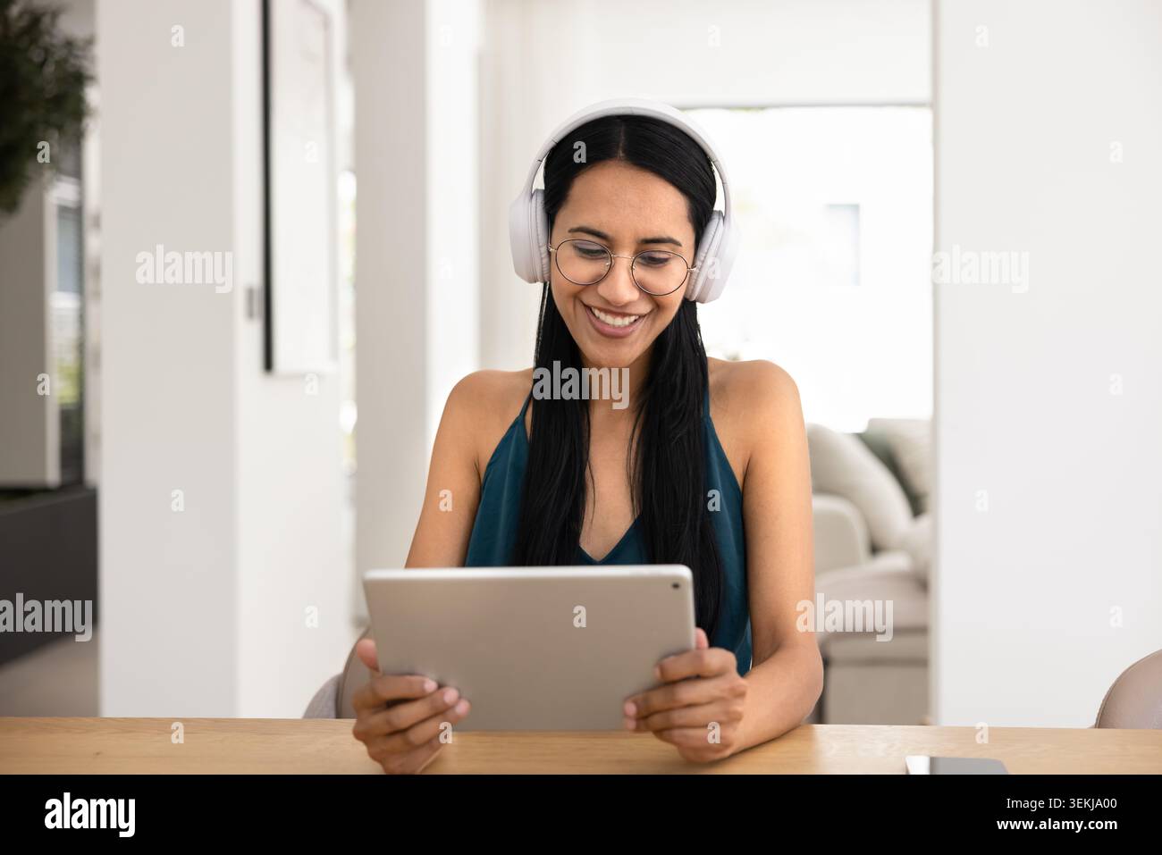 Junge Frau mit schnurlosen Kopfhörern, die zu Hause ein Tablet verwendet Stockfoto