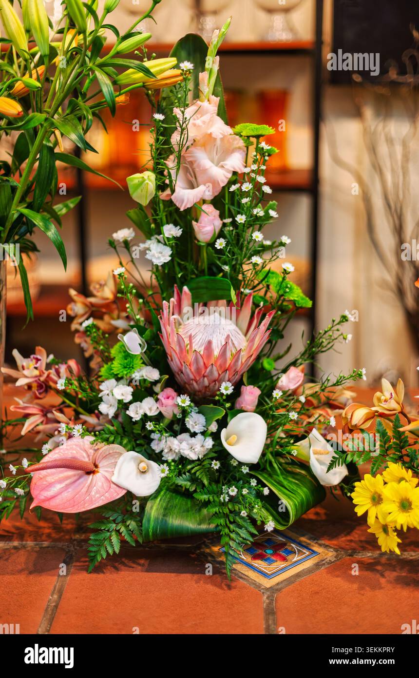 Herzstück mit einer markanten Königs-Protea-Blume, weißen Calla-Lilien, rosa Anthurium und Gladiolus-Stielen, die mit Grün auf einem Florist Sho angeordnet sind Stockfoto