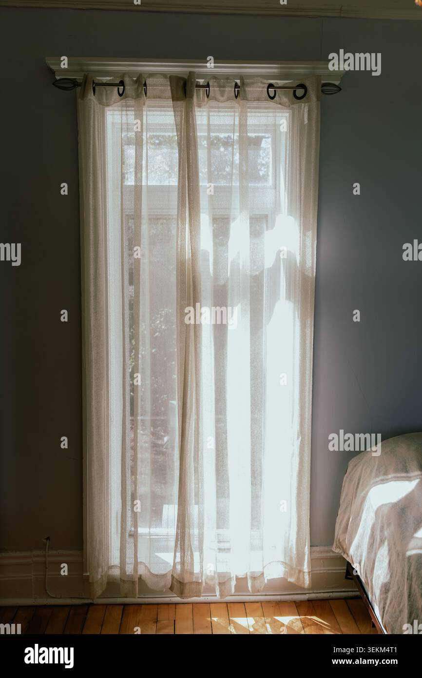 Blick auf ein Fenster mit weißem Vorhang auf einer Stange, von innen gesehen, mit natürlichem, sanftem Licht Stockfoto