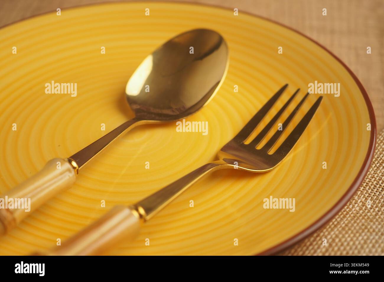 Goldene Utensilien auf einem gelben Teller, bereit für eine Mahlzeit Stockfoto