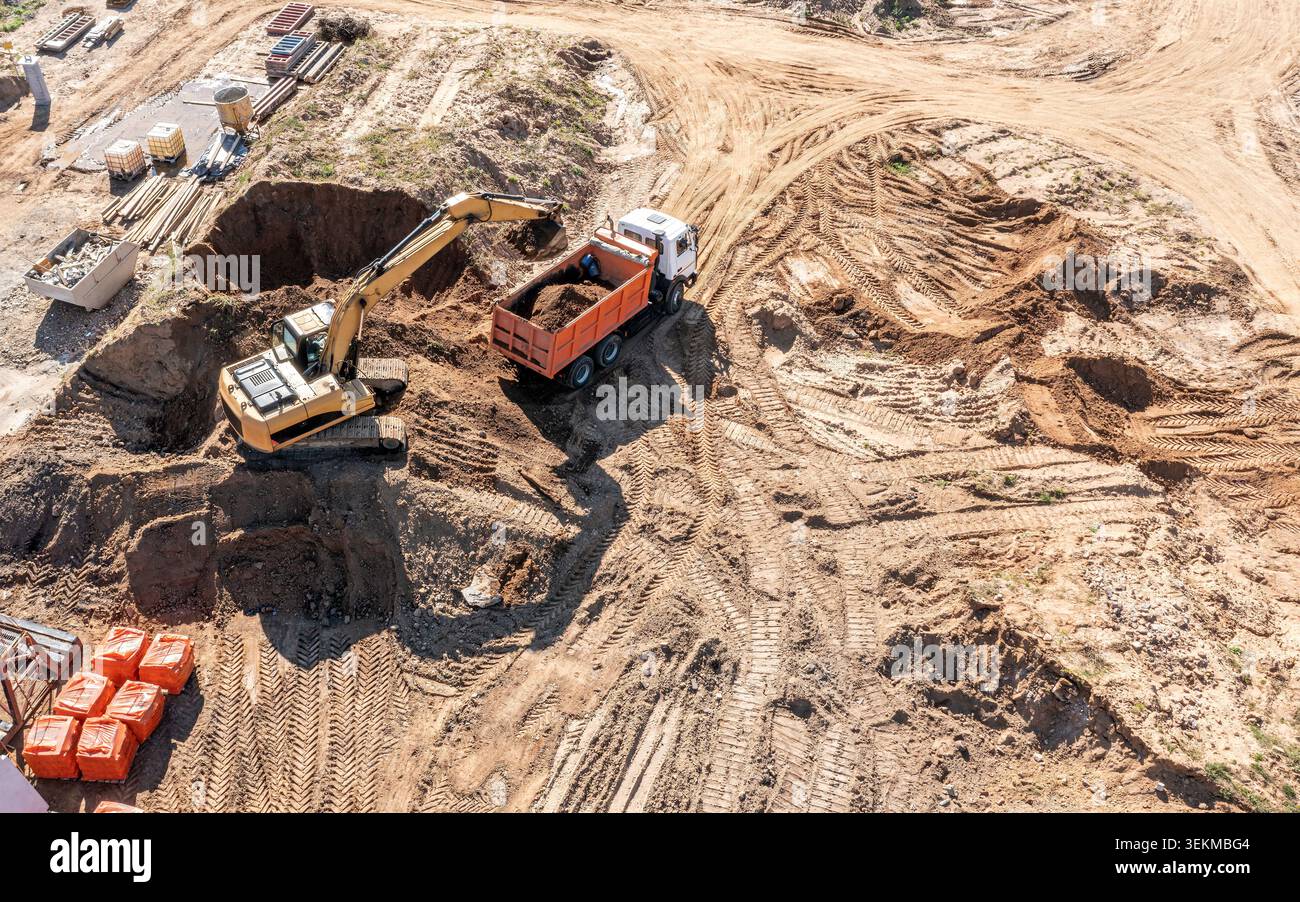 Der Laderbagger lädt Sand in einen Muldenkipper. Erdbewegung auf der Baustelle. Luftaufnahme. Stockfoto