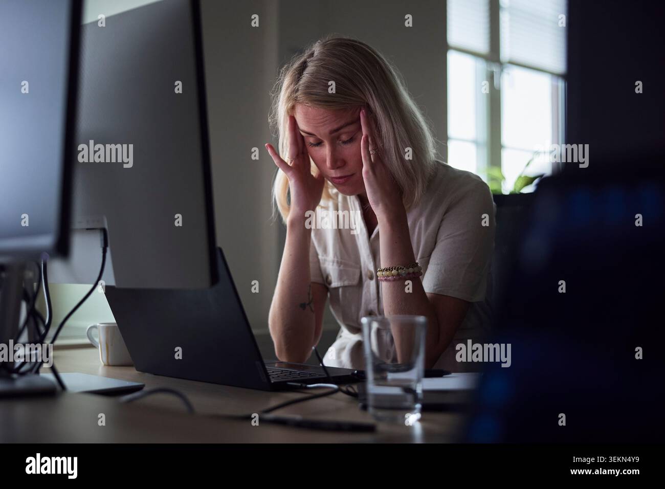 Erschöpfte junge Geschäftsfrau berührt die Tempel, während sie am Schreibtisch im Büro sitzt Stockfoto