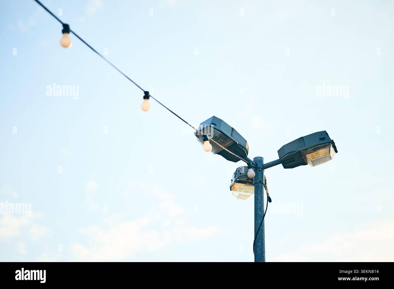 Ein hoher Stab mit montierten Flutlichtern und einer diagonalen Reihe hängender Lampen, die vor einem klaren, hellen Himmel gezeigt werden, schaffen eine einfache Außenbeleuchtung Stockfoto