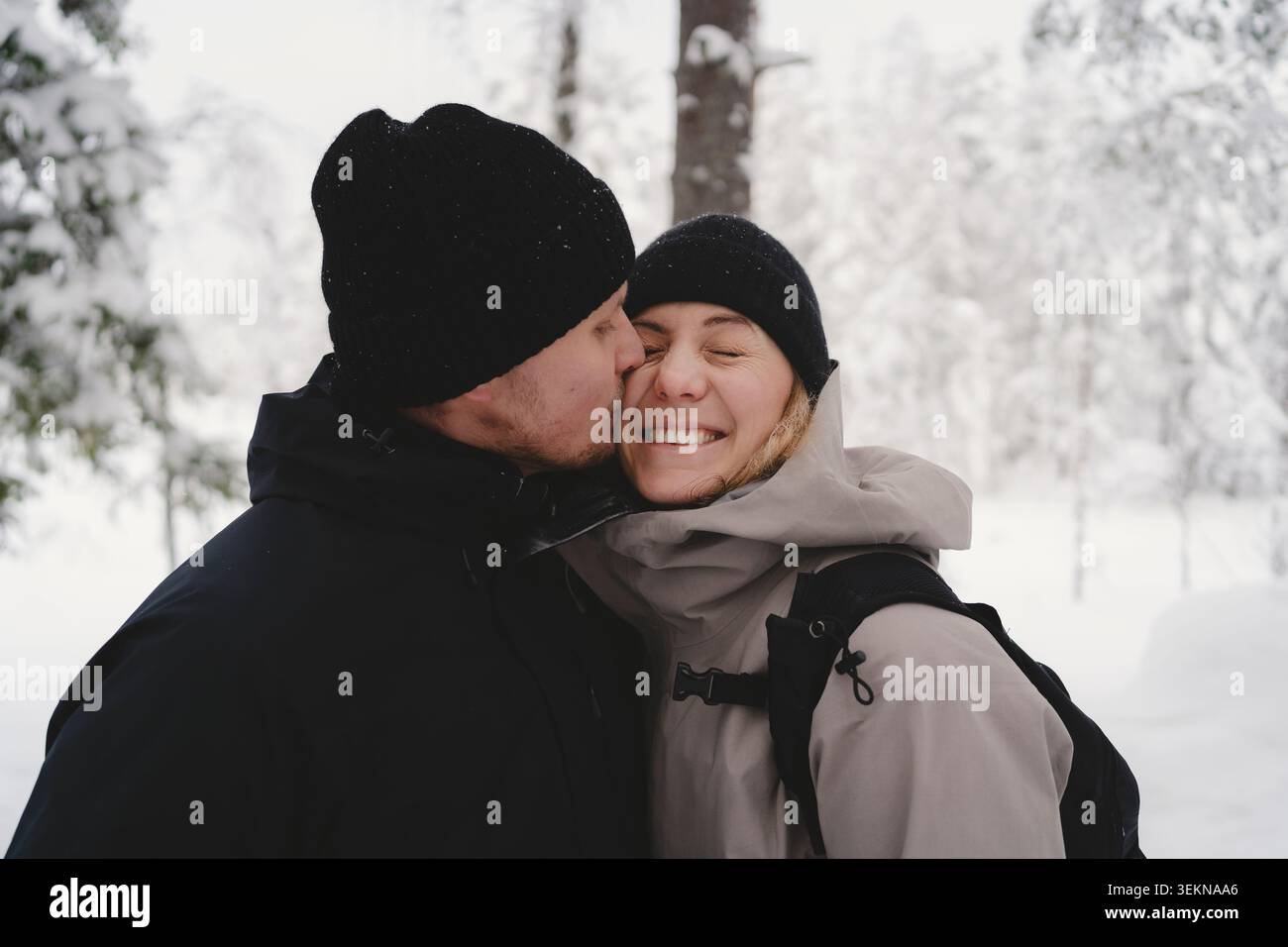Romantischer Mann, der eine Frau küsst, die Winterjacke im Wald trägt Stockfoto