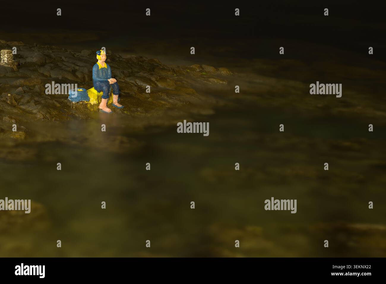 Statua di un uomo seduto sulla costa rocciosa di Trabia, Palermo, Sizilien. Suggestiva veduta notturna sul Mare con riflessi e luci soffuse. Stockfoto