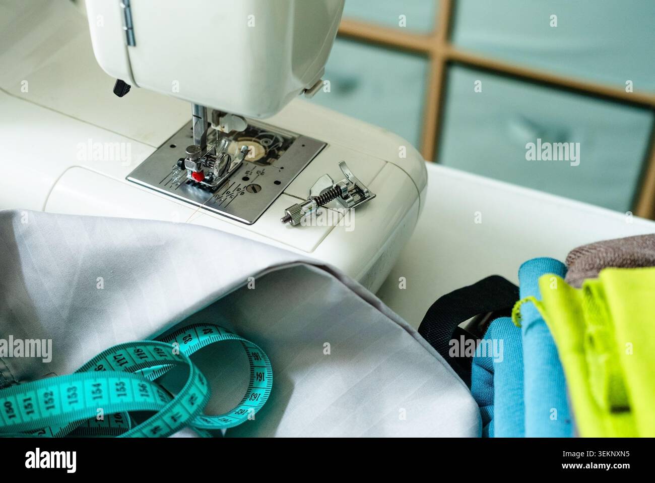 Nähmaschine auf weißem Basteltisch für funktionellen Arbeitsplatz. Nähmaschine mit Nähausrüstung für praktisches Basteln. Heimnähstation mit Werkzeugen und Zubehör für Heimarbeit Stockfoto