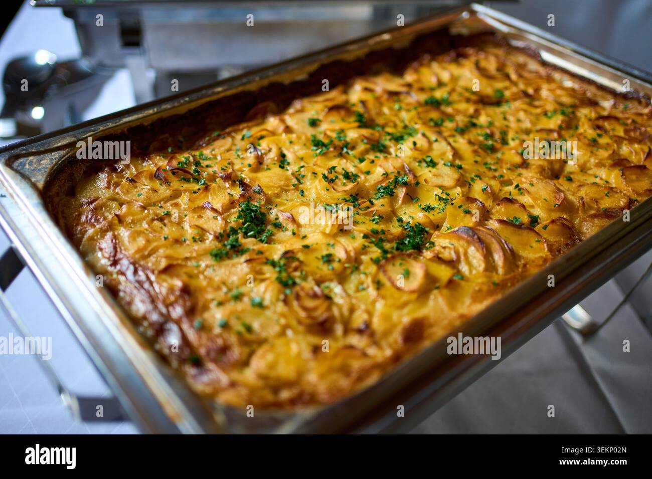 Cremiger Kartoffelgratin mit goldener Kruste und frischen Kräutern in einer Scheuerform. Stockfoto