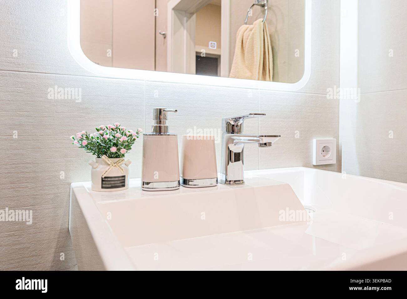 Modernes Badezimmer mit weißem Waschbecken, Chromarmatur und eleganten Accessoires. Die Beleuchtung ist hell und unterstreicht das klare Design. Stockfoto