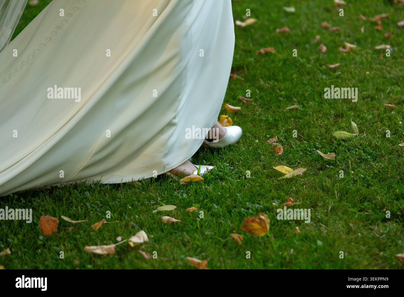 Braut geht auf grünem Gras mit gefallenen Blättern, trägt ein weißes Hochzeitskleid und Schuhe Stockfoto