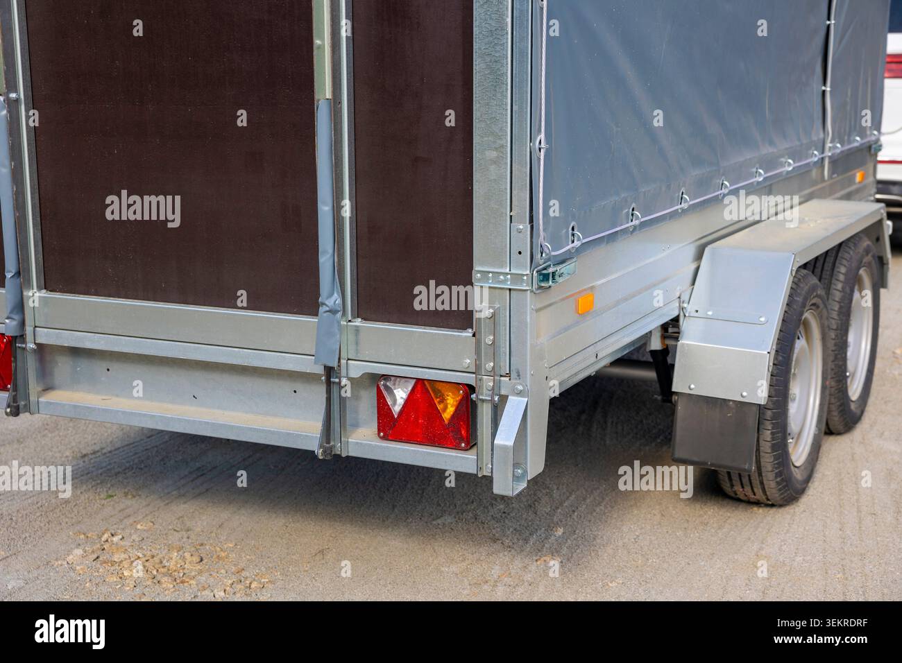 Nahaufnahme der Rückleuchten eines zweiachsigen Laderaumanhängers und der grauen Leinwandabdeckung. Konzept: Transportlogistik Stockfoto