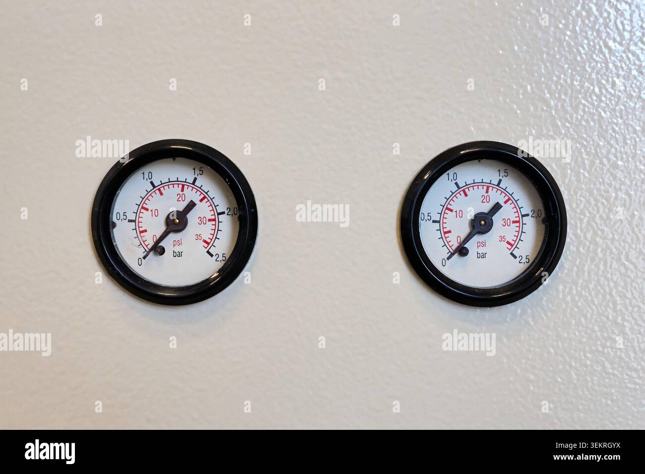 Zwei kreisförmige analoge Manometer mit schwarzen Rahmen nebeneinander auf einer sauberen weißen Oberfläche montiert. Stockfoto