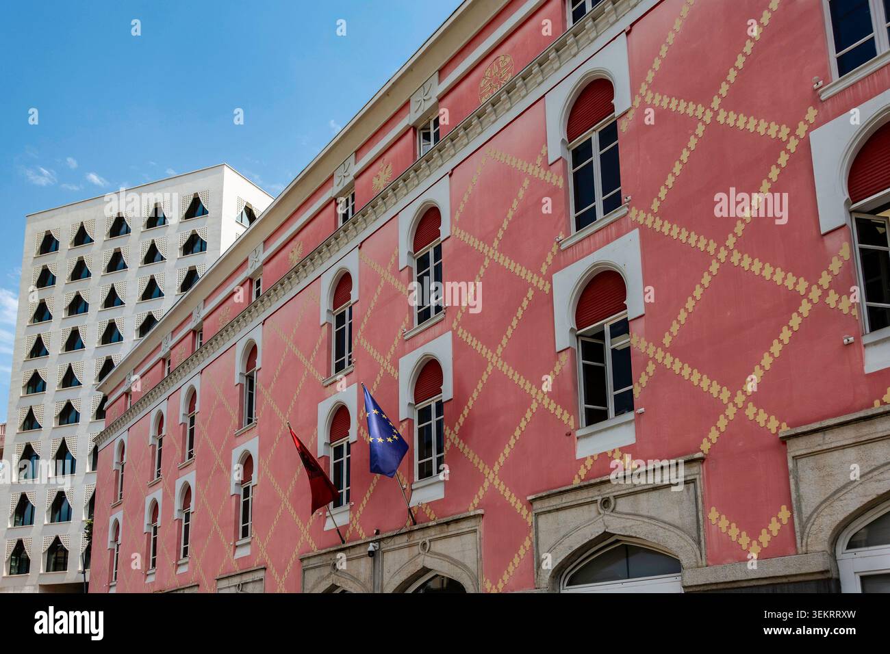 Die pinkfarbene Fassade des Ministeriums für Infrastruktur und Energie zeigt gelbe Gittermuster und Fahnen in Tirana, Albanien. Stockfoto