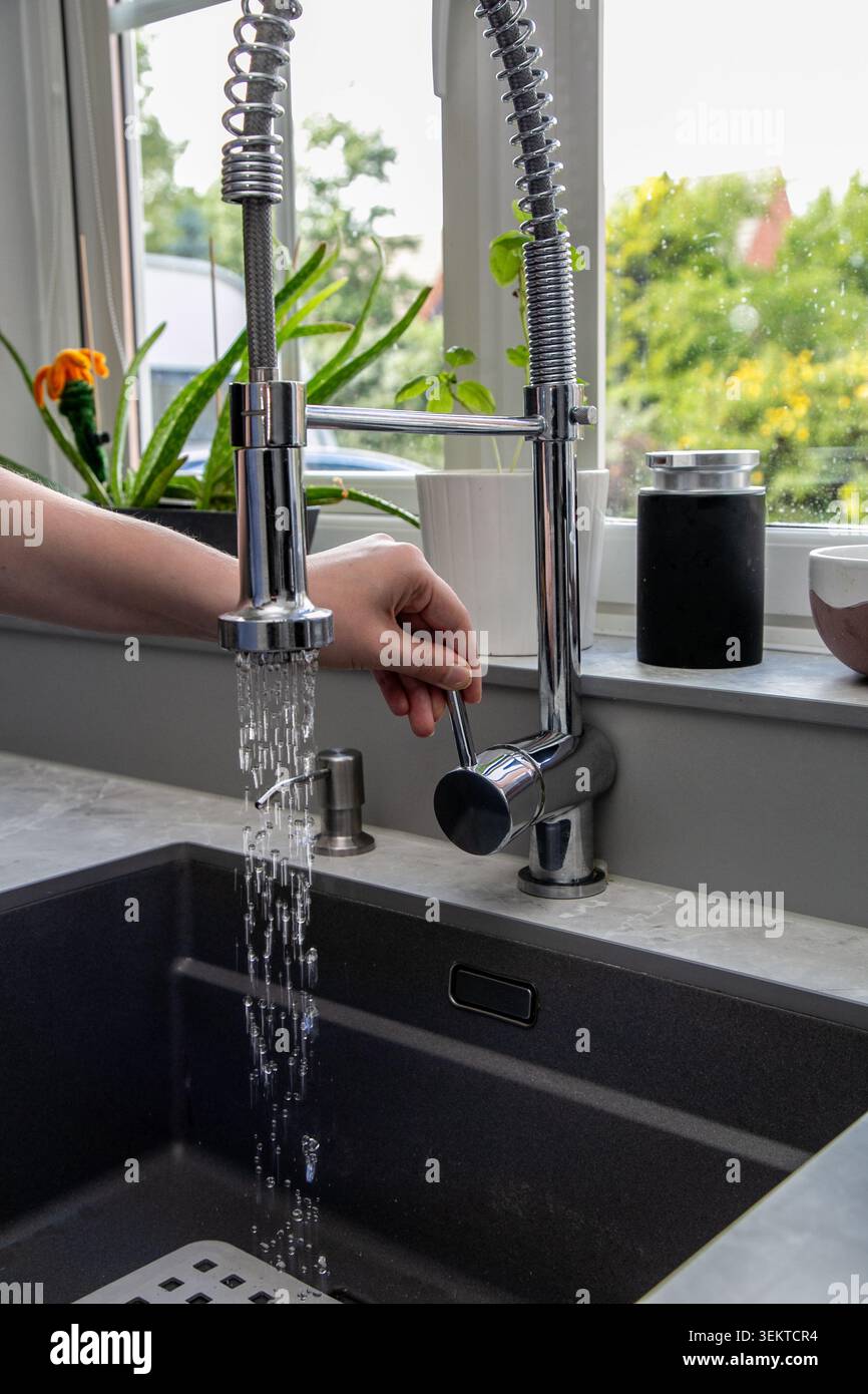 Nahaufnahme einer Person, die den Wasserhahn mit einem modernen Küchenarmatur mit polierter Chromoberfläche und integriertem herausziehbarem Spritzschlauch ein- oder ausschaltet. Stockfoto