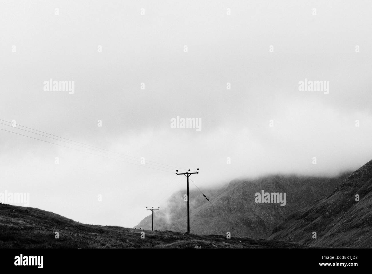 Dramatische monochrome Landschaft aus hölzernen Strommasten auf einem Hügel mit niedrigen Wolken und Nebel, die die Berge in Schottland bedecken Stockfoto