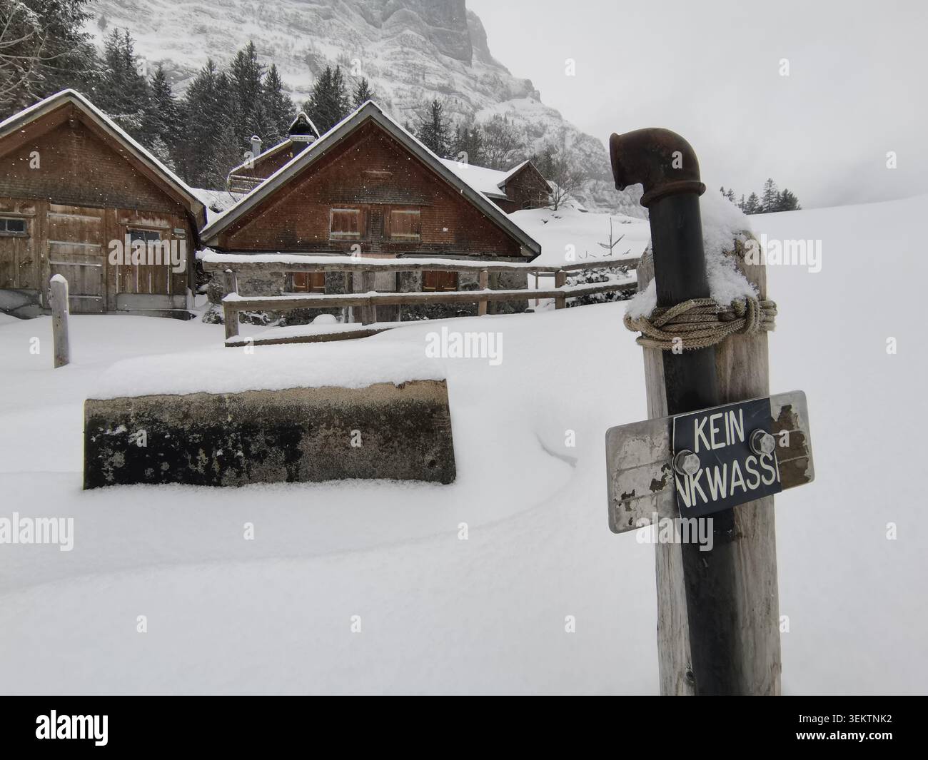 Schließen Sie einen Holzpfosten mit einem deutschsprachigem Schild mit der Aufschrift kein Trinkwasser neben einem tief verschneiten Holzchalet-Dorf im Winter Stockfoto