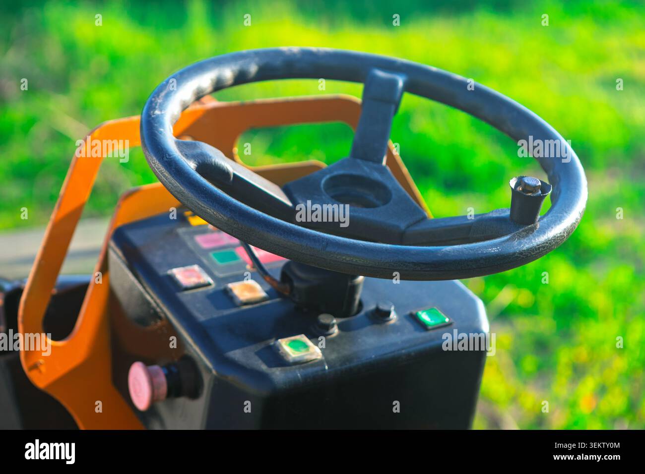 Das offene Cockpit einer industriellen Straßenwalze zeigt ein Lenkrad mit schwarzem Drehknopf. Auf orangefarbenem Chassis, kompaktes Konsolenhaus Stockfoto