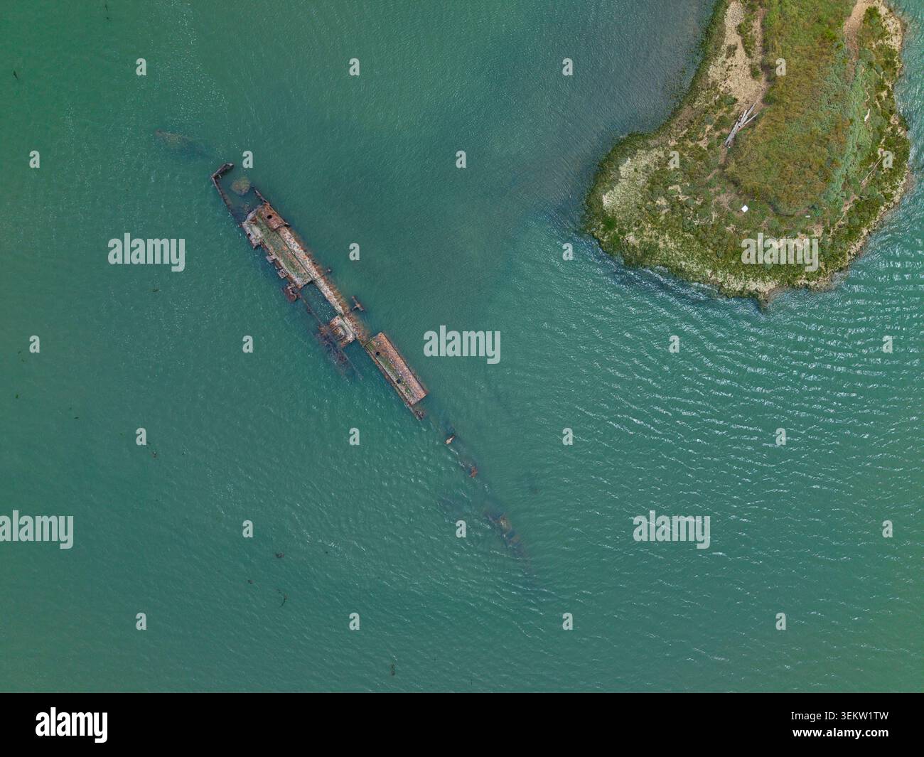 Aus der Vogelperspektive sehen Sie die rostigen Überreste des deutschen U-Boot-Wracks, die in den flachen grünen Gewässern der Mündung in der Nähe eines grasbewachsenen Ufers im Fluss Medwa liegen Stockfoto