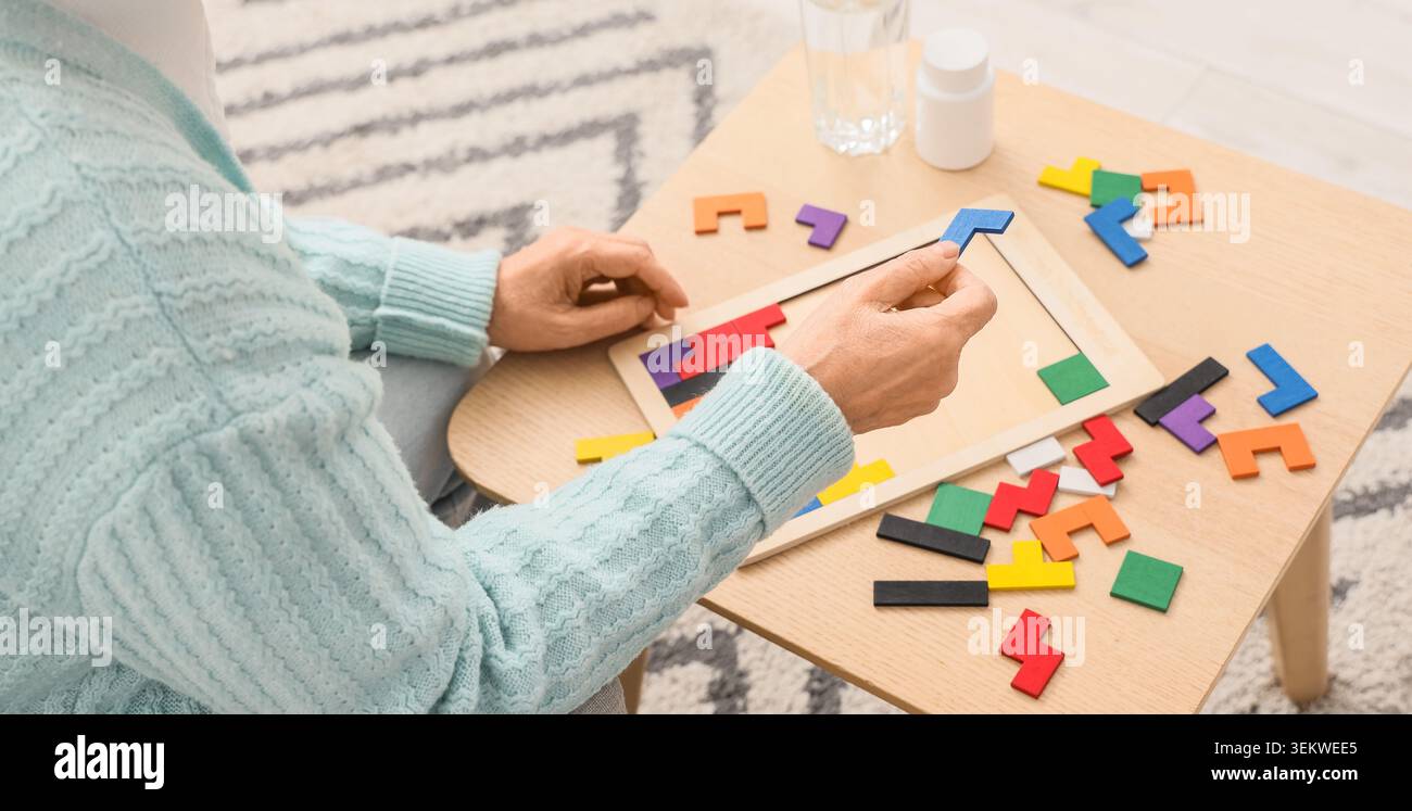 Seniorin löst buntes hölzernes Tangram-Puzzle zu Hause, Nahaufnahme der Hände während des Gehirntrainings für Gedächtnis, Konzentration und kognitive Fähigkeiten Stockfoto