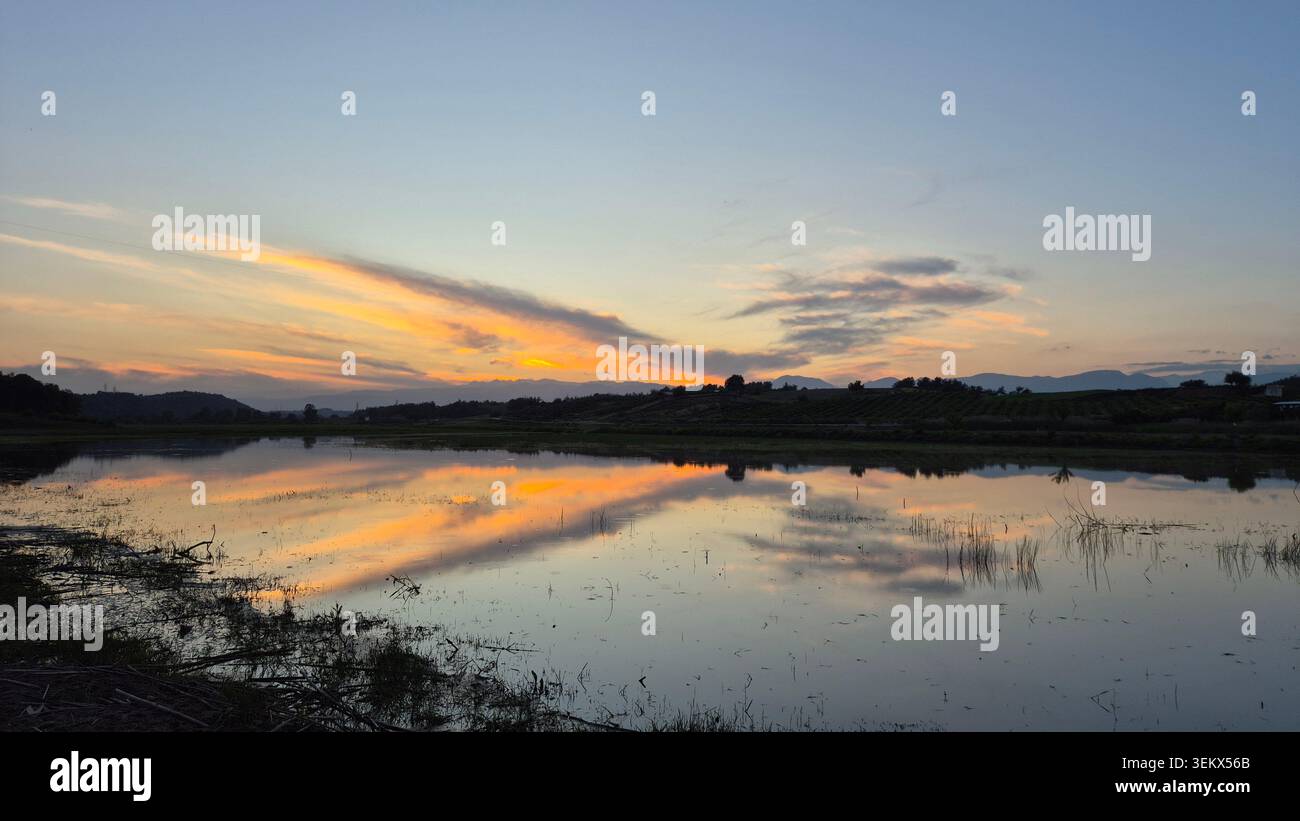 Ruhige Landschaft bei Sonnenuntergang mit lebendigen Himmelsreflexen auf der ruhigen Wasseroberfläche bei Dämmerung - Smartphone-aufgenommenes Stockfoto