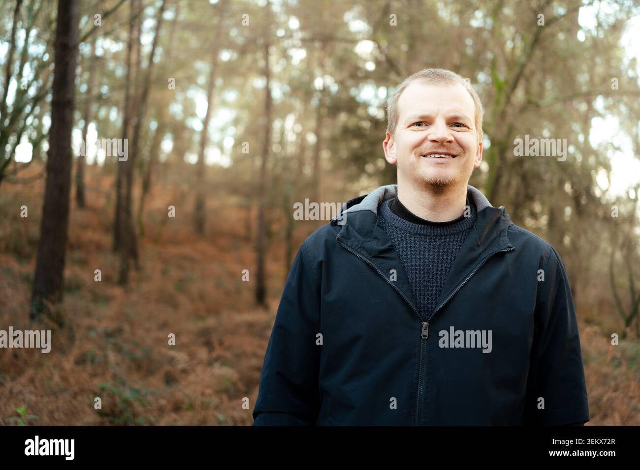 Ein Mann lächelt direkt in die Kamera und genießt einen ungezwungenen Tag im Freien beim Spazierengehen im Wald Stockfoto