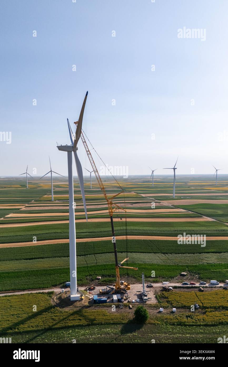 Installation von Windkraftanlagen mit einem großen Baukran. Der Montageprozess des Turbinenturms und der Rotorblätter. Luftaufnahme. Stockfoto