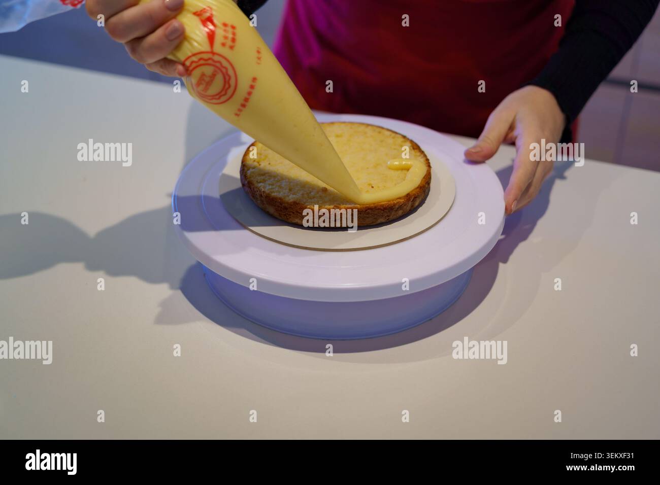Die Hände tragen Creme Frosting auf eine gebackene Kuchenschicht mit einem Paspelbeutel auf Stockfoto