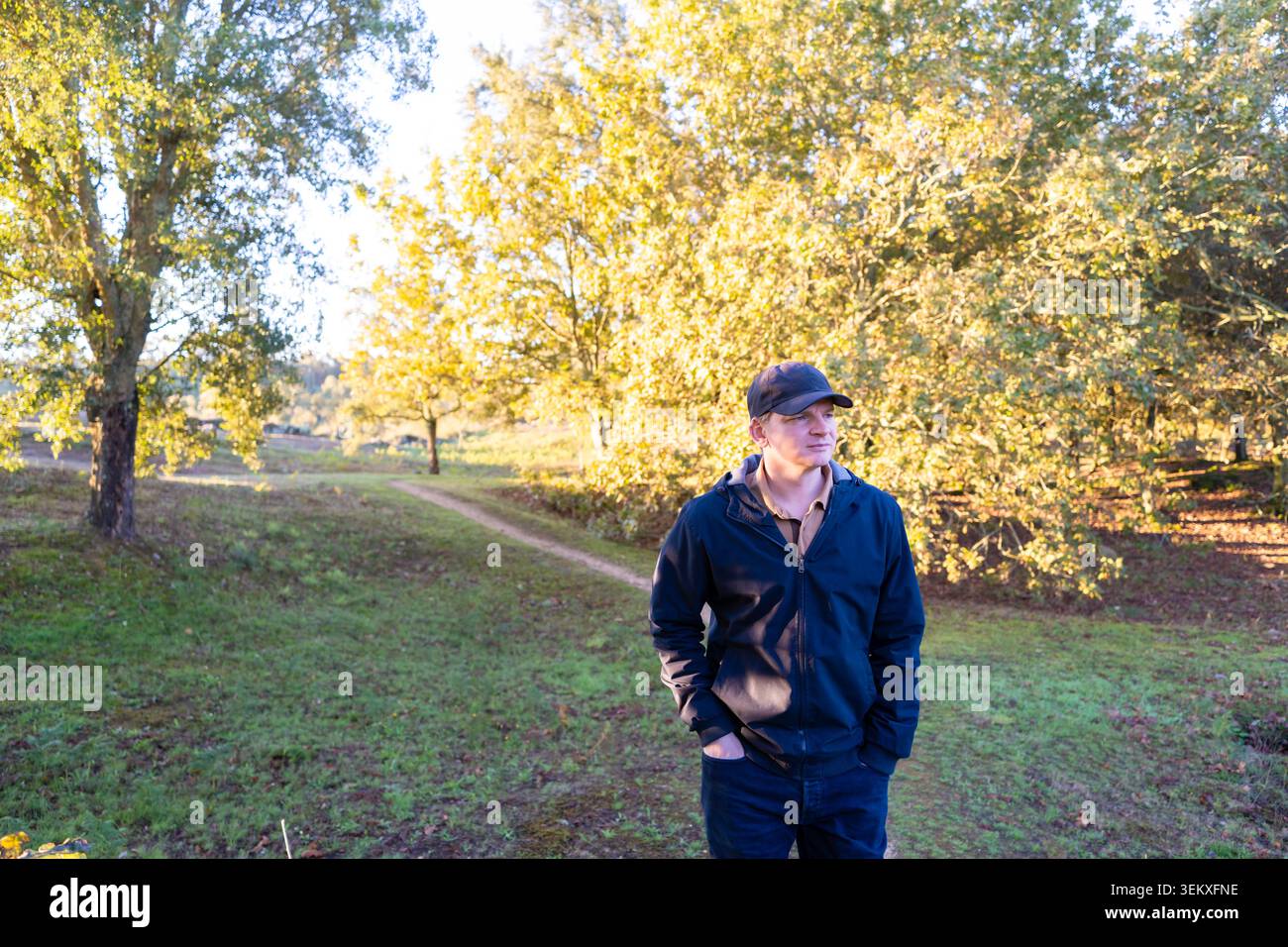 Mann mit Mütze und Jacke, der im Herbst in einem Park steht und die Natur bewundert Stockfoto