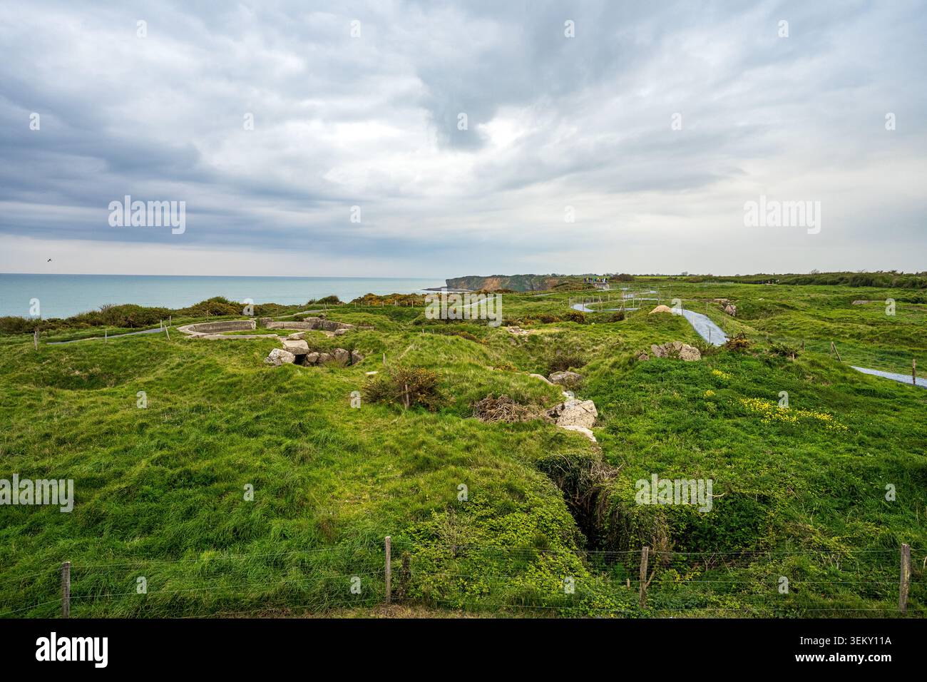 Weiter Blick auf Pointe du hoc mit Blick auf das Meer. Die grasbewachsene Kraterlandschaft bietet Betonbunkerruinen, Gräben und lange graue Wanderwege für VI Stockfoto