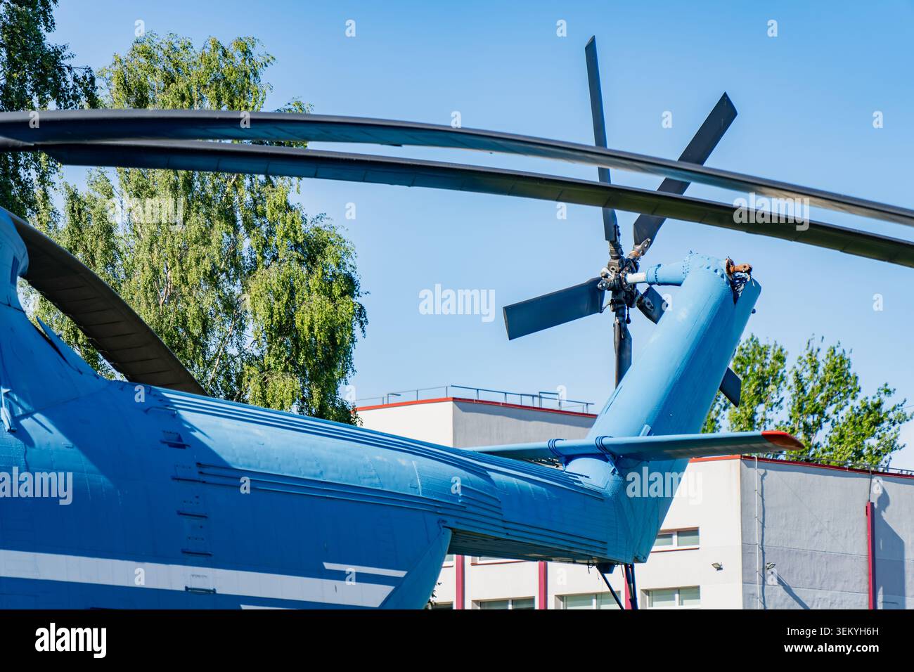 Schwere Helikopter-Heckkonstruktion mit grünen Bäumen und Gebäudefassade, die Investitionen auf dem nationalen Verteidigungsmarkt und Anlagen der Luftwaffe veranschaulicht Stockfoto