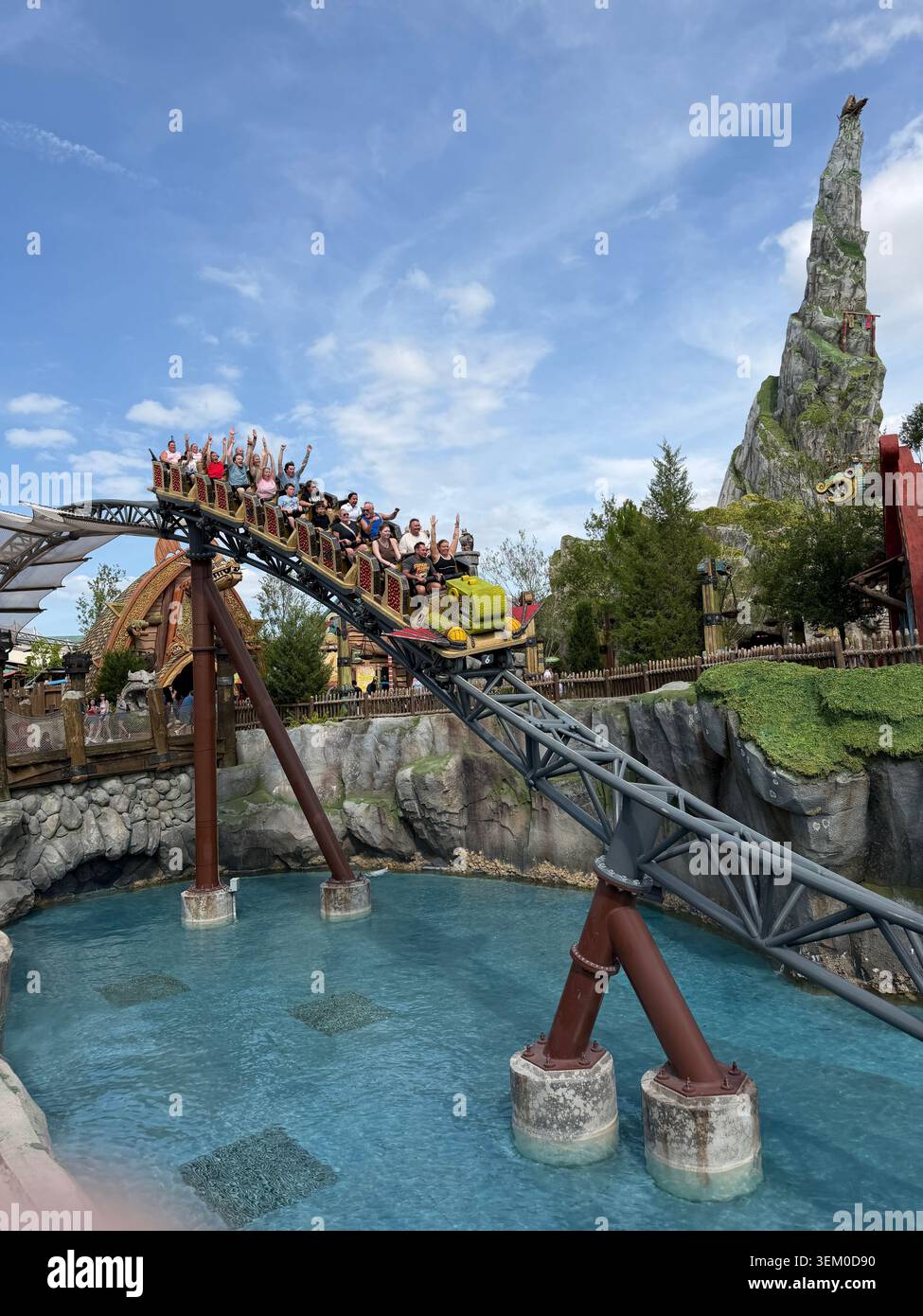 ORLANDO, FL - 3. JUNI 2026: Anfeuernde Fahrer fliegen auf der Achterbahn Hiccup's Wing Gliders im Epic Universe Orlando über eine hellblaue Lagune. - Smartphone-aufgenommenes Stockfoto