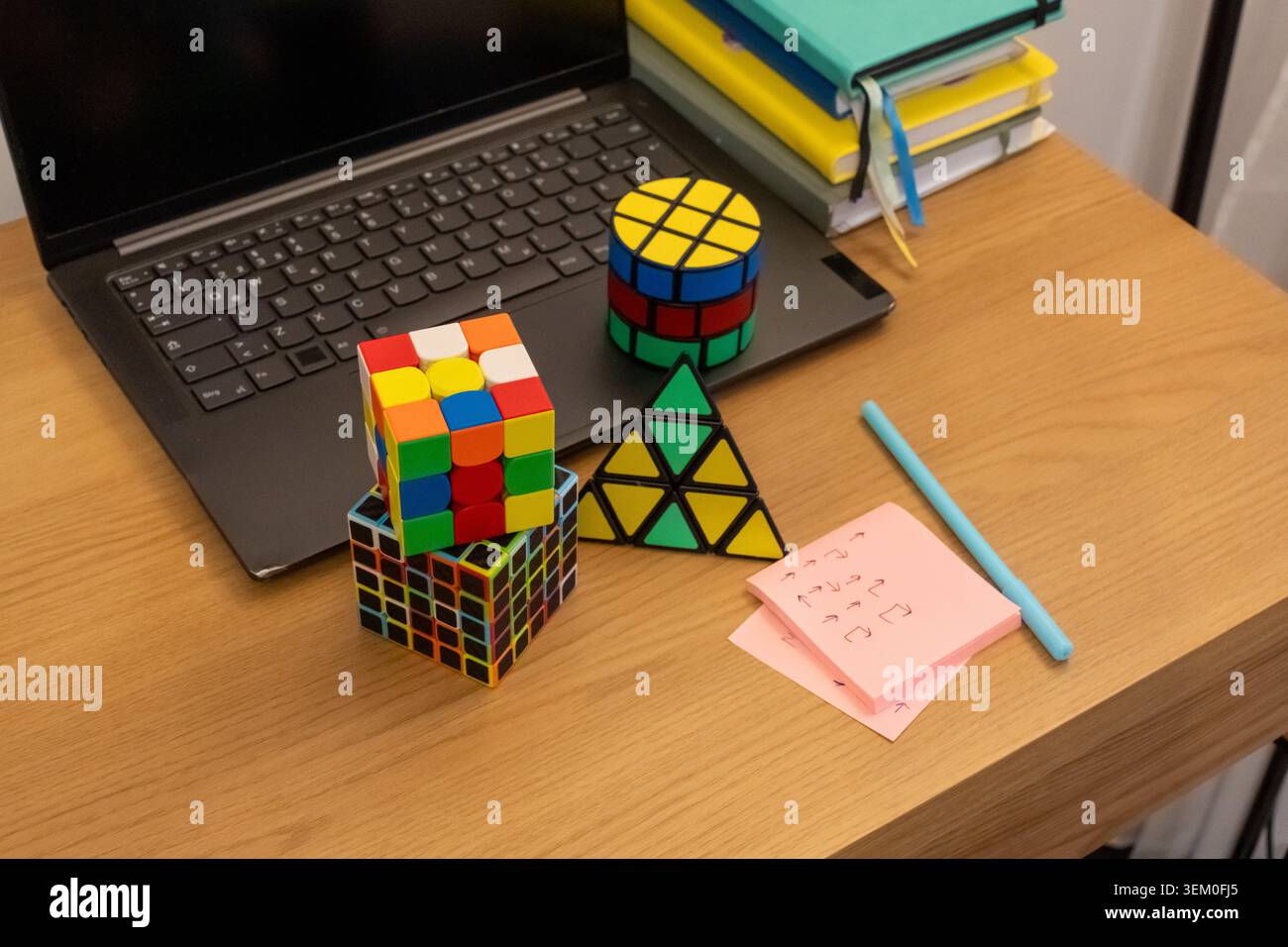Bunte 3D-Logikpuzzles Würfel, Pyramide und Zylinder auf Holzschreibtisch mit Laptop und handgeschriebenen Notizen. Konzept der intellektuellen Herausforderung, Gehirn Stockfoto