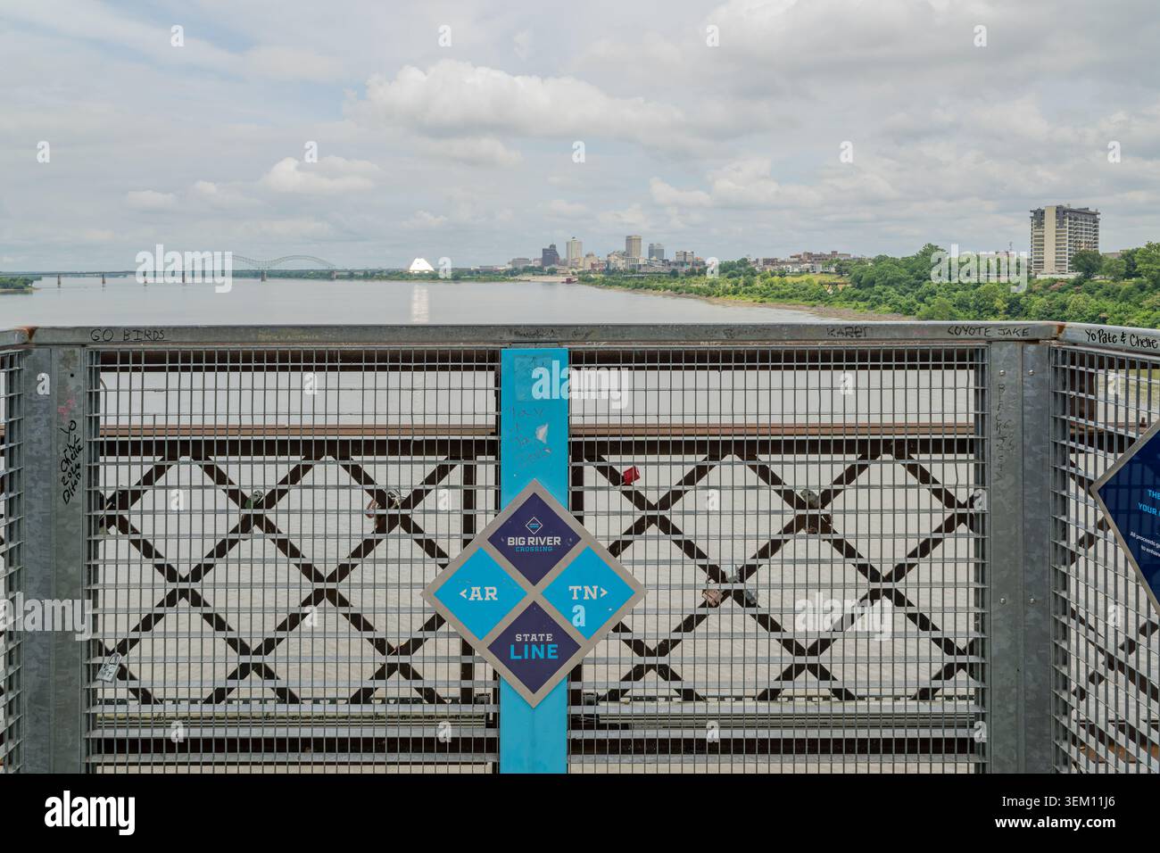 Ein blau-violettes Schild, das die Grenze zwischen Arkansas und Tennessee markiert, befindet sich auf einem Metallgeländer mit einer Skyline und einem Fluss in der Stadt Stockfoto