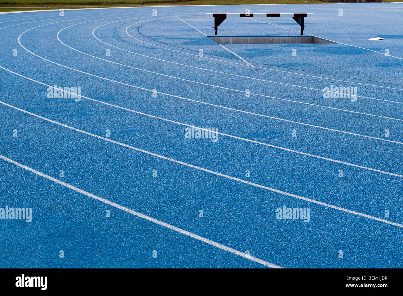 Leere blaue Laufstrecke mit Wassersprung und Fahrspurmarkierungen in einem Leichtathletikstadion. Stockfoto