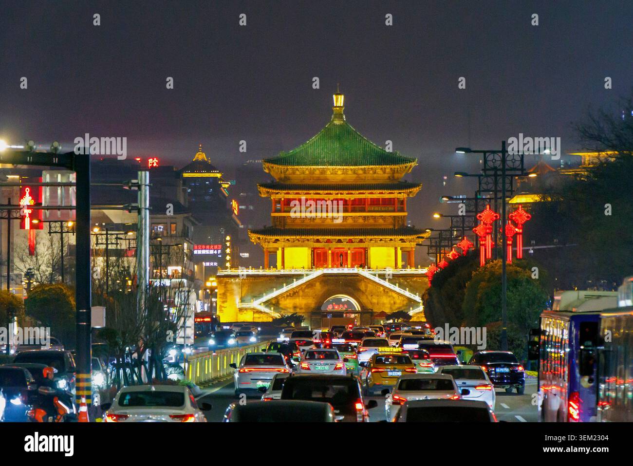 Der Nachtverkehr fließt in Richtung des beleuchteten Glockenturms im Zentrum von Xi'an, China, mit roten Festdekorationen an der Straße. Stockfoto