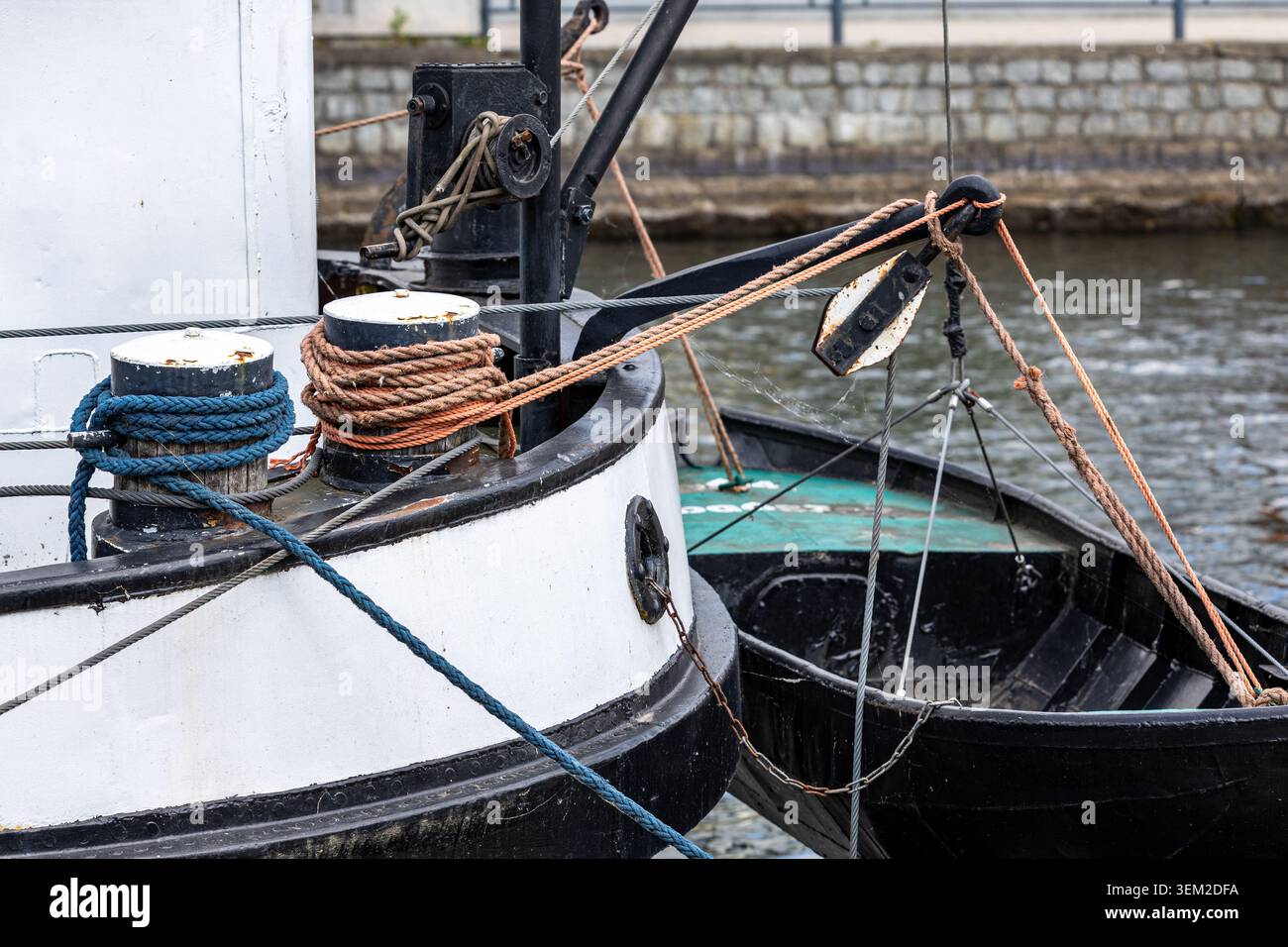 Sternabschnitt eines vertäuten Bootes mit blauen und braunen Seilen, die um Metallpfoller gewickelt sind. Zusätzliche Leitungen verlaufen durch Riemenscheiben und Klammern Stockfoto