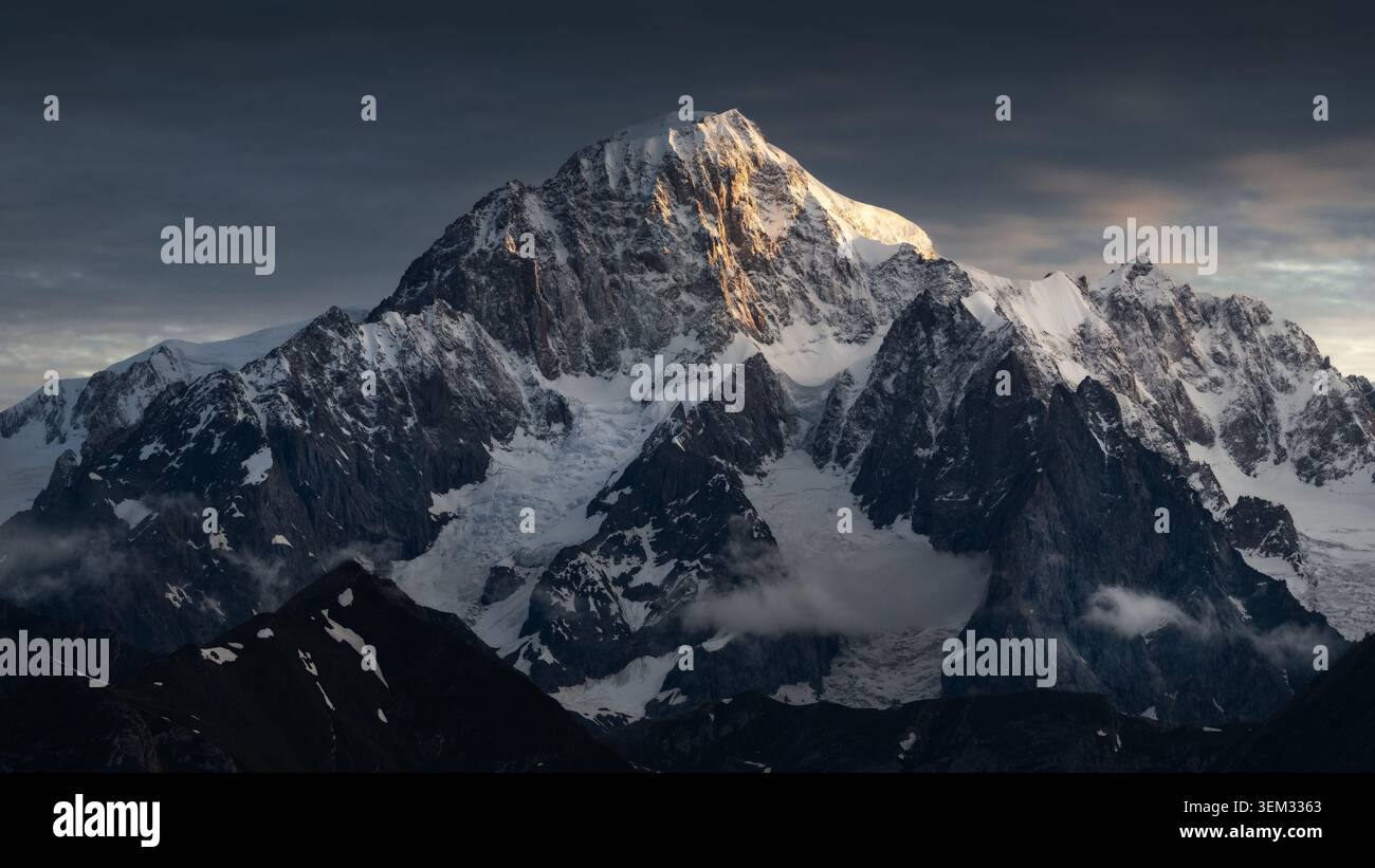 Blick auf die majestätischen schneebedeckten Gipfel des Mont Blanc-Massivs, beleuchtet durch goldenes Sonnenuntergangslicht unter einem dramatischen Himmel im Aostatal, Italien. Stockfoto