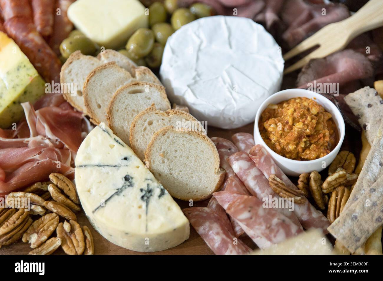 Aus nächster Nähe auf eine Gourmet-Wurstplatte mit Brie-Käse, geschnittenem Baguette-Brot, Salami und Pekannüssen. Stockfoto