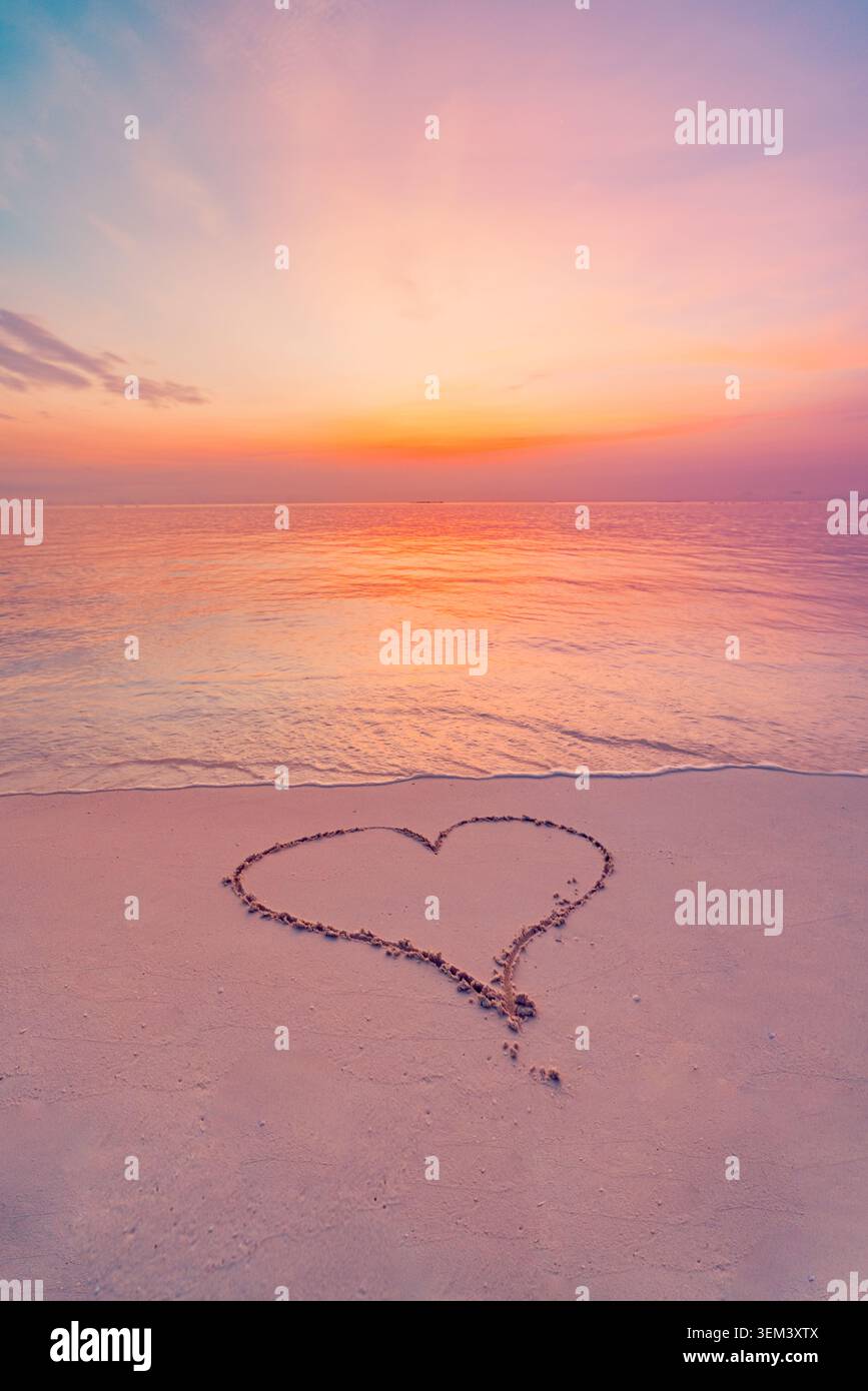 Herzform im Sand am Strand bei weichem pastellfarbenem Sonnenuntergang am ruhigen Meer gezogen. Liebe Romantik Flitterwochen. Sommerstrandurlaub Reisen Urlaub Valentinstag Paradies Stockfoto