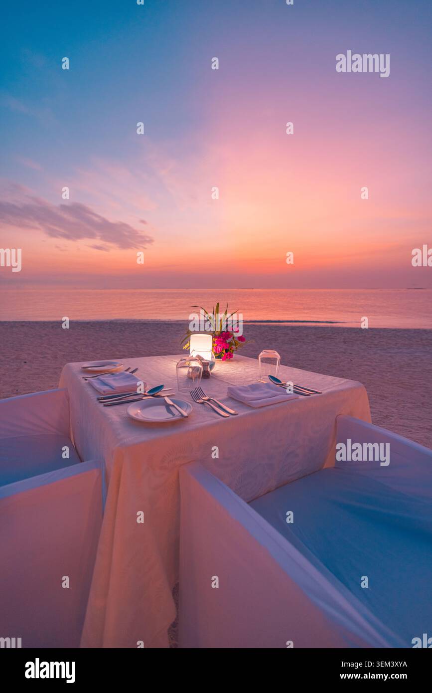 Kerzenbeleuchteter romantischer Strandabendtisch für zwei bei tropischem Sonnenuntergang. Meeresblick rosa Himmel Flitterwochen. Luxus Sommerreise Urlaub Ausflug Feier Stockfoto