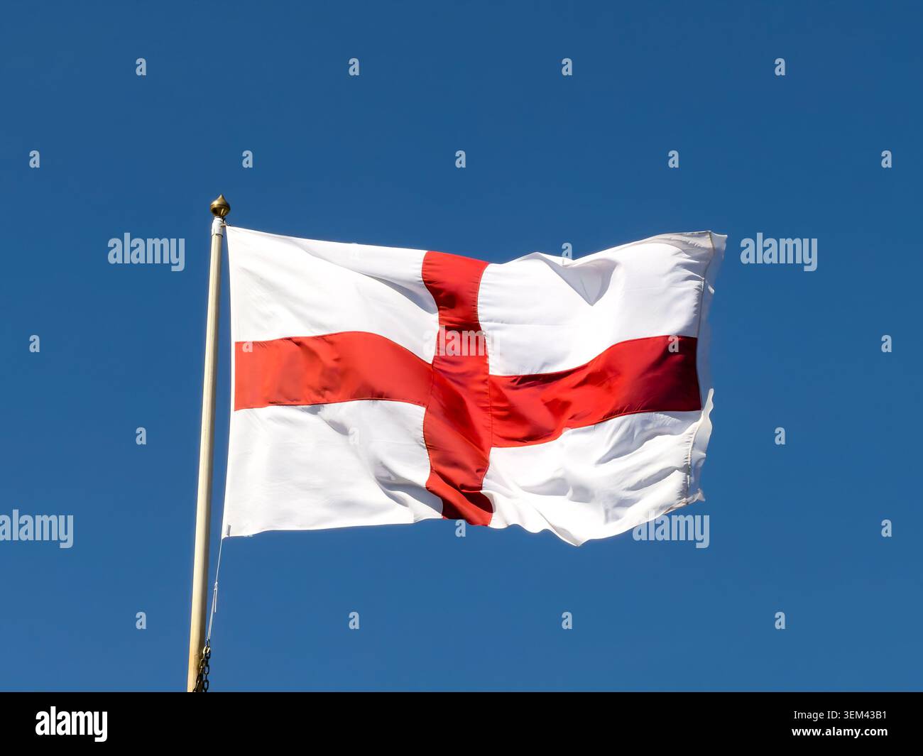Die englische Flagge des St. George's Cross fliegt vom Fahnenmast aus und zeigt das weiße und rote Kreuz vor dem Hintergrund des blauen Himmels in England Stockfoto