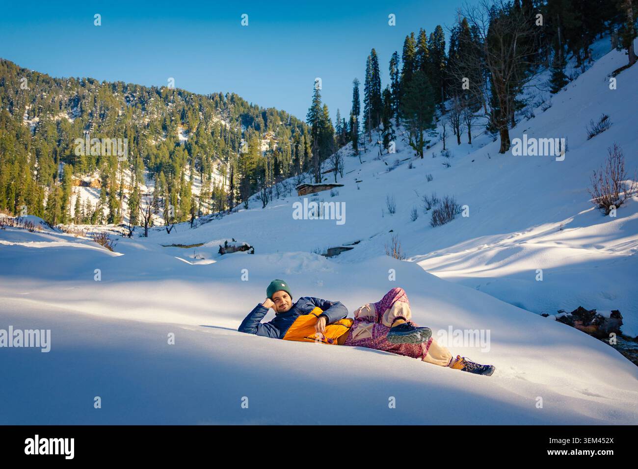 Ein Mann liegt auf tiefem Schnee in einem wunderschönen Bergtal, umgeben von Kiefern in Kaschmir, Indien. Stockfoto