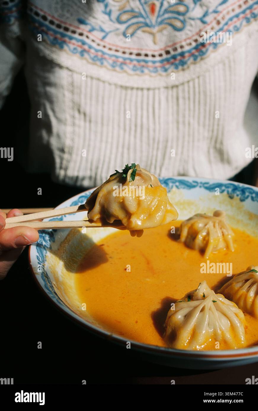 Eine Person, die einen momo-Knödel aus einer cremigen Sauce hebt Stockfoto