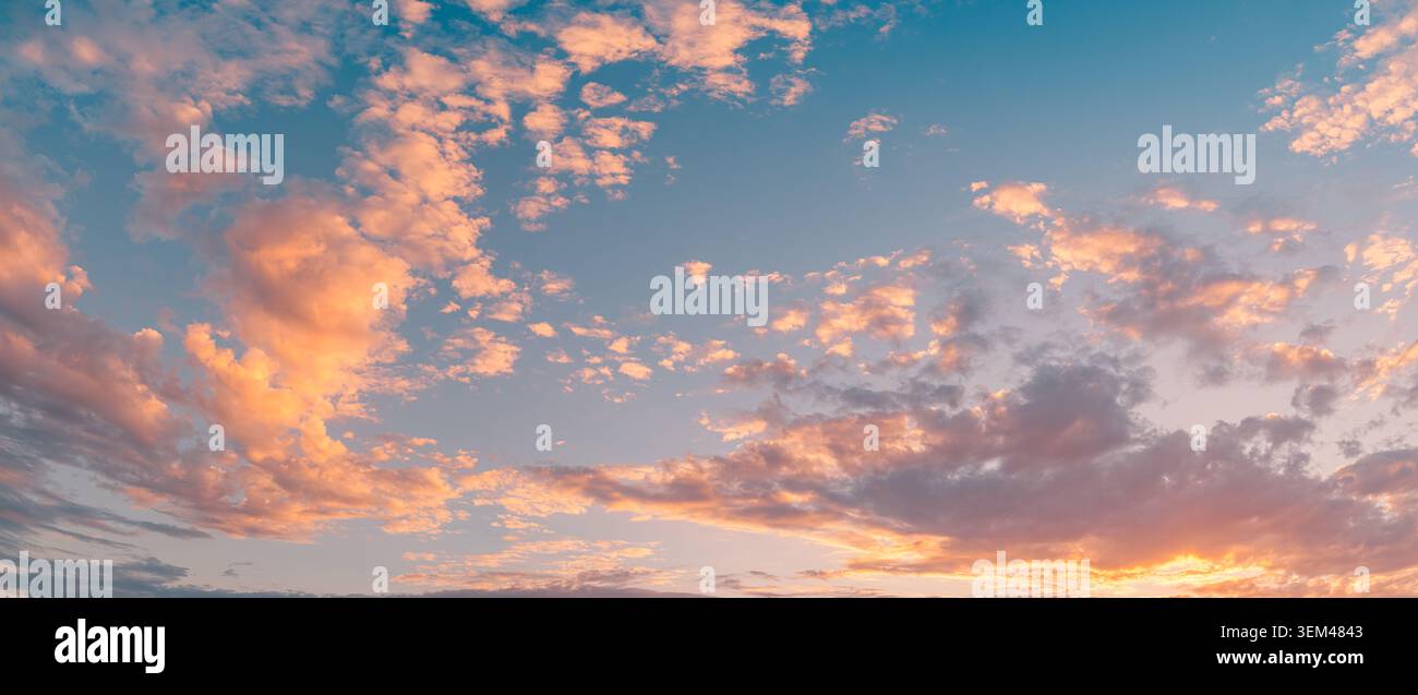 Atemberaubende weite Sonnenuntergangshimmel-Panorama mit pastellrosa Wolken und Sonnenstrahlen über dem Horizont. Abendliche Sommer-Wolkenlandschaft. Hintergrund-Wallpaper-Design, malerisch Stockfoto