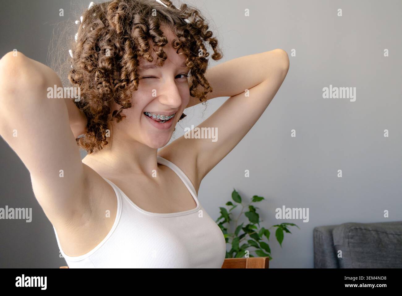 Porträt eines verspielten Teenager-Mädchens mit Wattestäbchen im Haar während des hitzefreien Lockenvorgangs zu Hause. Natürliche Haarstylemethode, DIY-Schönheitsroutine, Prepar Stockfoto