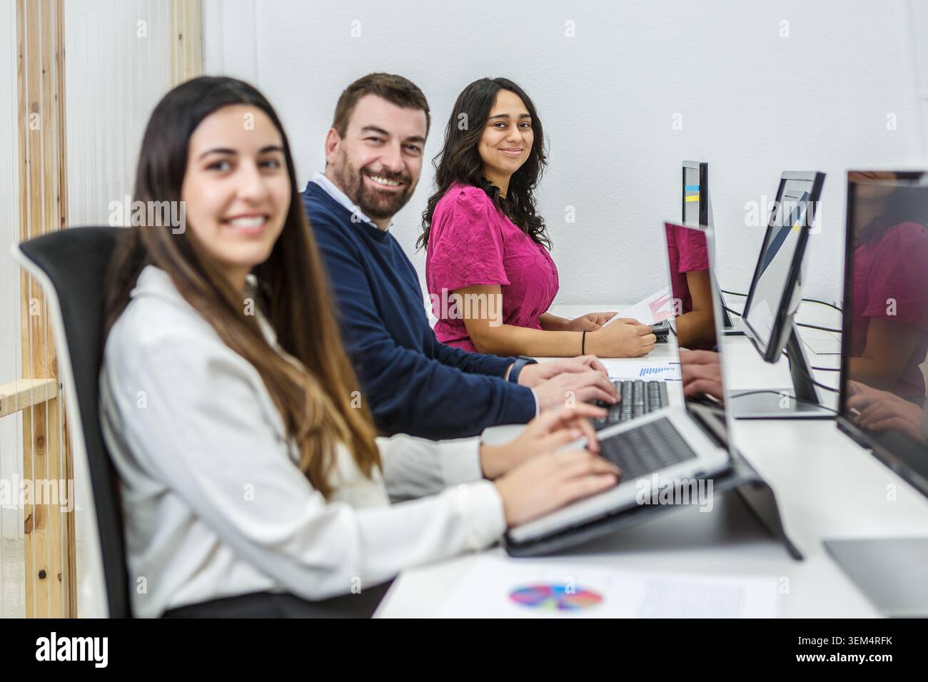 Drei Personen konzentrieren sich auf ihre Computer in einem Coworking Space. Diese Szene findet tagsüber in einer modernen Büroumgebung statt. Stockfoto