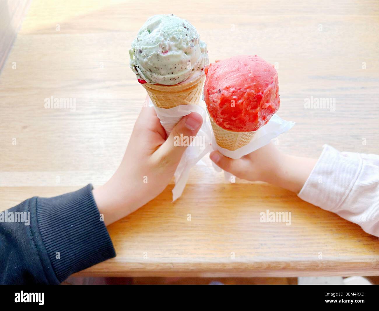 Zwei Kinder halten bunte Eiswaffeln zusammen auf einem Holztisch im Sommer Stockfoto