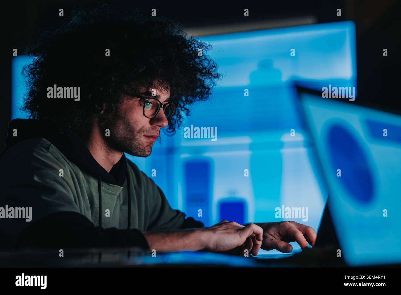 Junge Profis, die spät an einem Notebook arbeiten und Daten mit Teamkollegen auf mehreren Bildschirmen analysieren Stockfoto