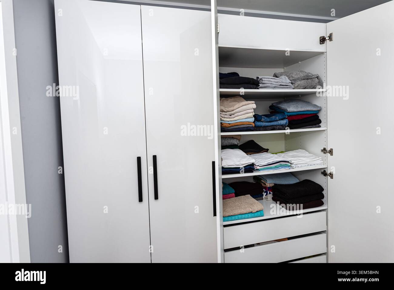 Offener weißer Kleiderschrank mit Regalen mit organisierter gefalteter Kleidung Stockfoto