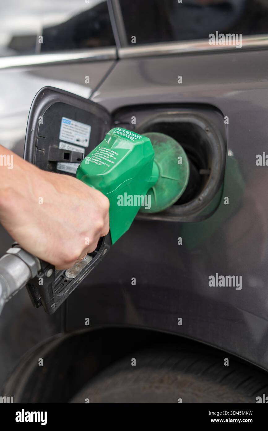 Ein hochwertiges Nahaufnahme-Foto, das eine aus der Perspektive einer Hand zeigt, die eine grüne Kraftstoffpumpe in den Tank eines Autos einführt. Die Aufnahme h Stockfoto