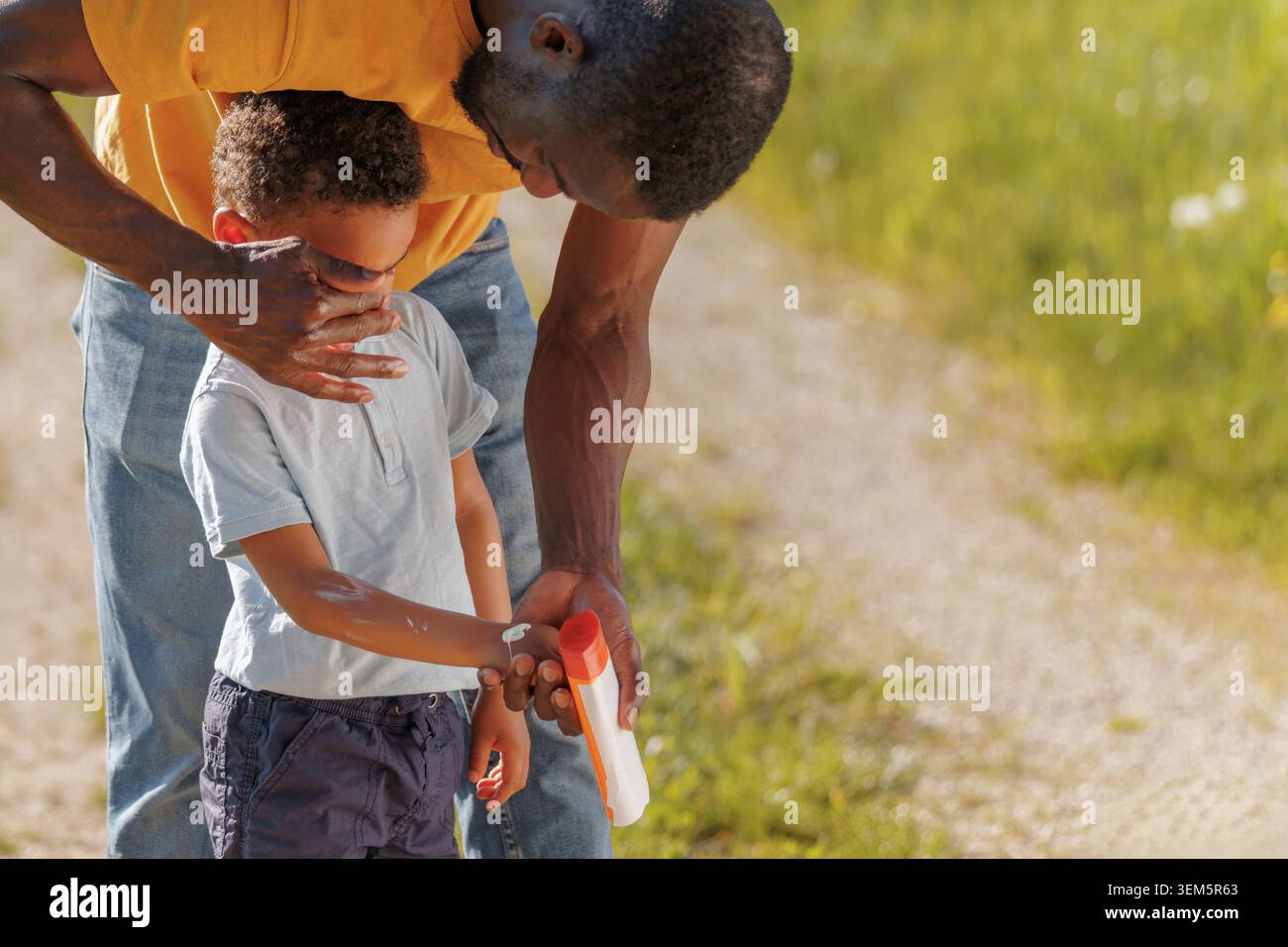 Vater hilft seinem Sohn mit Sonnencreme, seine Haut unter der hellen Sonne zu schützen, während er die Zeit der Familie im Freien gemeinsam in der Natur genießt. Stockfoto